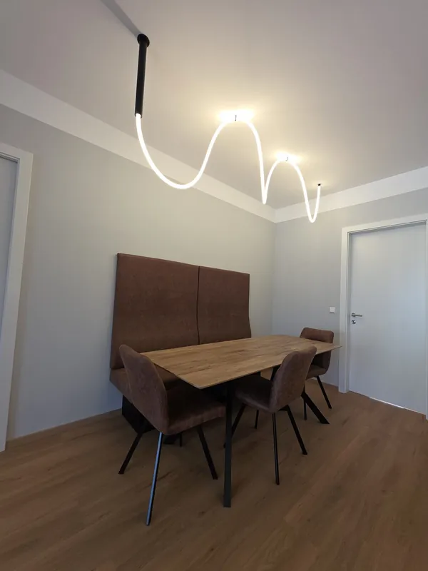 Essplatz mit raumhoher, gepolsterter Sitzbank, Holztisch und Leuchte an der Decke